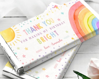 Puede incluir: Envoltorio de barra de chocolate con temática de arcoíris con el texto "THANK YOU FOR MAKING MY BIRTHDAY BRIGHT" y "love. Amanda". El envoltorio presenta un arcoíris de acuarela, un sol y estrellas sobre un fondo blanco con lunares de colores.