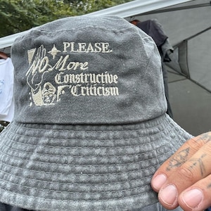 May include: A gray bucket hat with the text "PLEASE. No More Constructive Criticism" embroidered on the front.