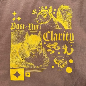 May include: A brown t-shirt with a yellow graphic design featuring two squirrels, the text "Post-Nut Clarity", and various nuts including a peanut, acorn, and walnut.
