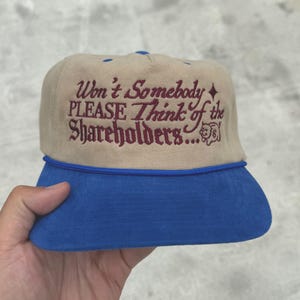 May include: Tan and blue trucker hat with the embroidered text "Won't Somebody PLEASE Think of the Shareholders...". The hat has a blue brim and a blue rope detail. The text is in a burgundy color.