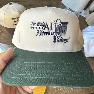 May include: A beige and green baseball cap with the text "The Only AI I Need is Clippy" embroidered on the front.