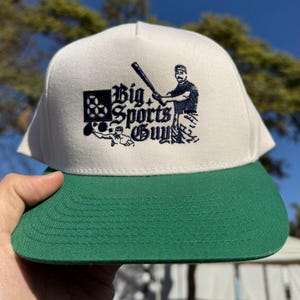 May include: White and green baseball cap with a navy blue embroidered logo that says "Big Sports Guy" and features a cartoon baseball player holding a bat.