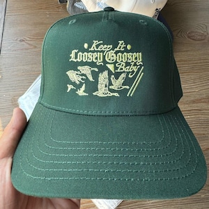 May include: A dark green baseball cap with a white embroidered design that says "Keep It Loosey Goosey Baby" with a graphic of flying geese.