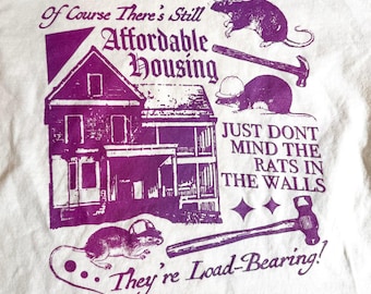May include: A white t-shirt featuring a purple graphic print of a house and three rats wearing construction hard hats. The text reads: Of Course There's Still Affordable Housing, JUST DONT MIND THE RATS IN THE WALLS, They're Load-Bearing!