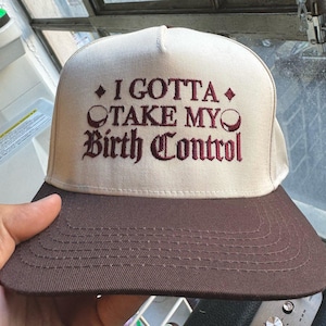 Könnte beinhalten: Eine beige und braune Baseballkappe mit dem Text "I gotta take my birth control", der in Maroon gestickt ist.