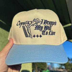 Peut inclure: Une casquette de baseball beige et bleu clair avec une image brodée d'une femme en maillot de bain et le texte "Oops I Dropped My Will To Live".