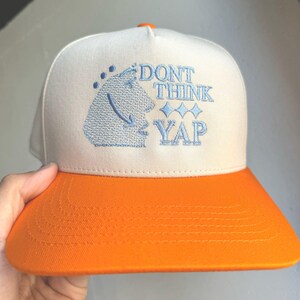 May include: A white and orange baseball cap with the text "DON'T THINK YAP" embroidered in blue on the front.
