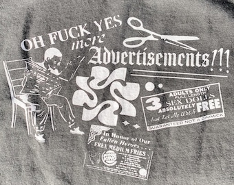 May include: A dark gray t-shirt featuring a white graphic print of a person reading a newspaper on a chair, a pair of scissors, and text that reads OH FUCK YES more Advertisements!!!, 3 ADULTS ONLY FULL LENGTH SEX DOLLS ABSOLUTELY FREE, and In Honor of Our Fallen Heroes... FREE MEDIUM FRIES.