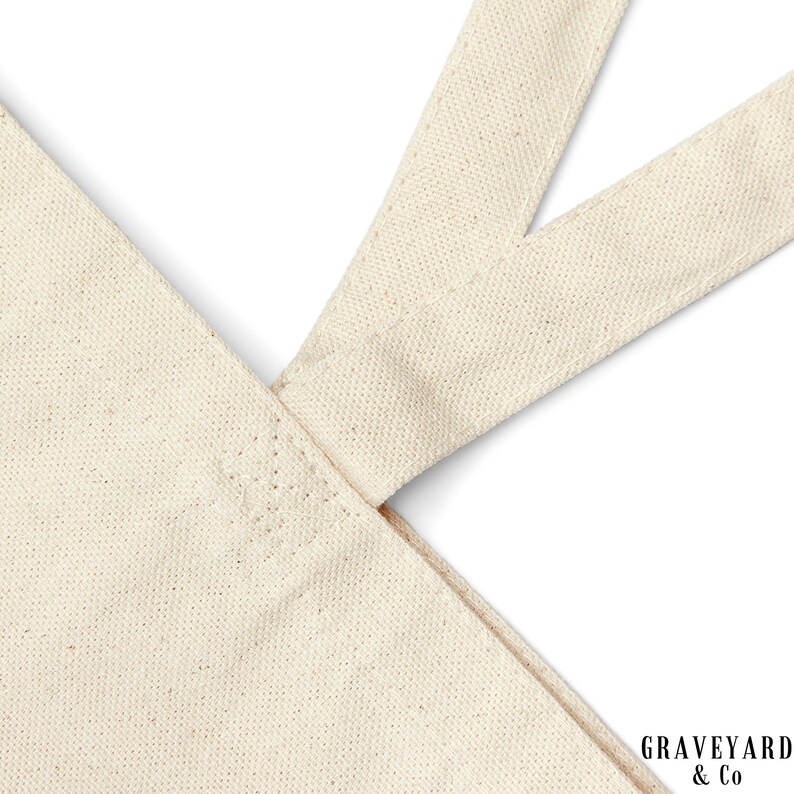 May include: Close-up of the top of a natural canvas tote bag with two straps. The straps are sewn together at the top of the bag. The bag is made of natural canvas and has a natural color.