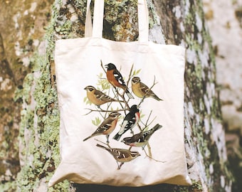 May include: A cream-colored canvas tote bag featuring a detailed illustration of seven various birds perched on thin brown branches with small green leaves. The bottom right corner of the bag displays the text Graveyard & Co in black font.