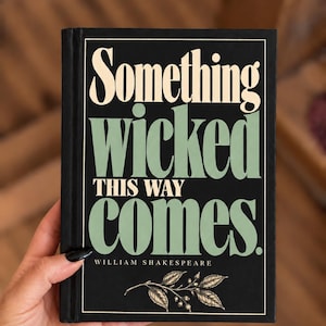 May include: A black book cover with the text Something wicked THIS WAY comes in cream and sage green lettering. The author name William Shakespeare is printed below in small white text, and a botanical illustration of a leafy branch sits at the bottom.