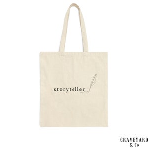 May include: A white canvas tote bag with black text that reads "storyteller" and a simple line drawing of a feather.