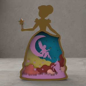 Puede incluir: Silueta de madera en capas de una princesa sosteniendo una varita de estrella. El vestido revela una escena con una luna creciente, un hada, un unicornio y nubes. La paleta de colores incluye dorado, rosa, turquesa y amarillo. Artículo decorativo.