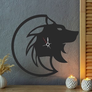 May include: A black metal wall clock in the shape of a wolf's head, set within a circular frame. The clock hands are red and white. The clock is mounted on a gray wall, with decorative elements in the foreground.