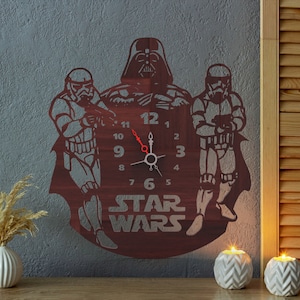 May include: A wooden wall clock featuring Darth Vader and two Stormtroopers. The clock hands are red, and the numbers are visible. The words "STAR WARS" are at the bottom of the clock.