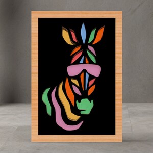 Puede incluir: Una impresión artística enmarcada que presenta una cabeza de cebra estilizada y colorida con gafas de sol. La cebra está compuesta por tonos vibrantes, incluyendo naranja, verde, rosa y azul, sobre un fondo negro. El marco es de madera clara.