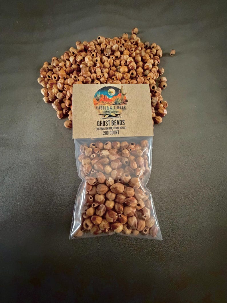 May include: A collection of small, light brown, natural juniper cedar beads, with a portion loose and a portion contained in a clear plastic bag. The bag features a tan paper header with the text Cactus & Timber, Ghost Beads, and 200 count.