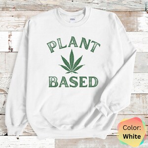 Puede incluir: Sudadera blanca con una hoja de marihuana verde y el texto "PLANT BASED" en una fuente desgastada.