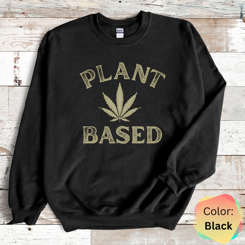 Puede incluir: Sudadera negra con una hoja de marihuana verde y el texto "PLANT BASED" en una fuente de estilo vintage.