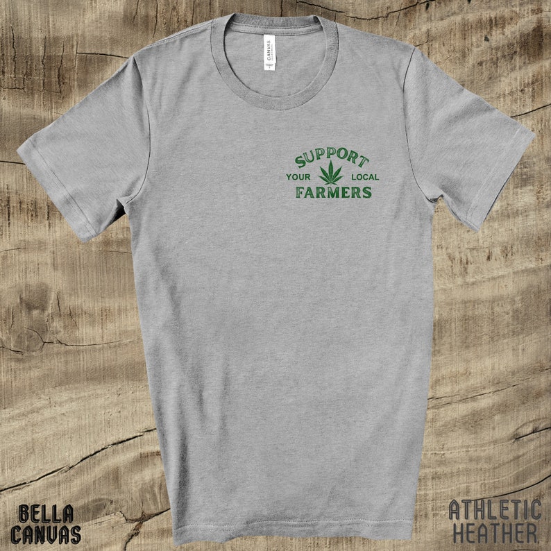 K&ouml;nnte beinhalten: Ein graues T-Shirt mit dem Text "Support Your Local Farmers" in gr&uuml;ner Schrift mit einer gr&uuml;nen Marihuana-Blattgrafik.