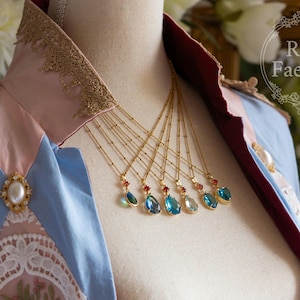 Könnte beinhalten: Eine Schaufensterpuppe trägt ein blaues und rosa Kleid mit Spitzenbesatz und eine goldene Halskette mit mehreren tropfenförmigen blauen und roten Edelsteinanhängern.