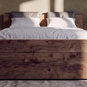 Puede incluir: Un marco de cama de madera rústica con una textura de grano de madera natural prominente, con una funda nórdica blanca y dos almohadas blancas. La cama está flanqueada por dos mesitas de noche de madera, cada una con una lámpara pequeña.