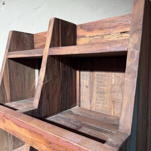 May include: A brown wooden storage unit featuring two open compartments on the top tier, constructed from reclaimed wood with visible grain patterns, rough textures, and a sturdy frame with angled side panels and a horizontal support beam.