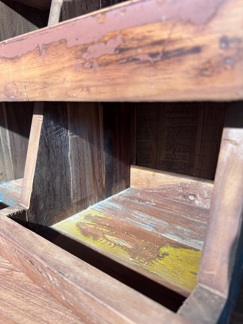 May include: A small wooden step stool featuring a weathered brown finish with visible wood grain. The structure includes a flat top surface and a lower step, with hints of yellow and blue paint showing through the distressed wood texture.