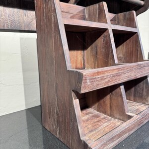 May include: A dark brown wooden tiered storage rack featuring four open compartments arranged in two rows. The unit has a slanted front design with visible wood grain texture and sturdy side panels, providing an open structure for organizing items.