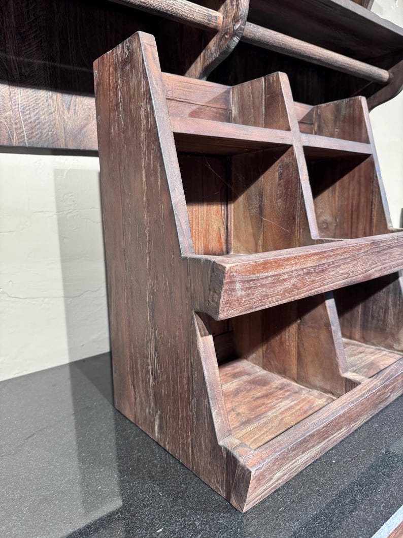 May include: A dark brown wooden tiered storage rack featuring four open compartments arranged in two rows. The unit has a slanted front design with visible wood grain texture and sturdy side panels, providing an open structure for organizing items.