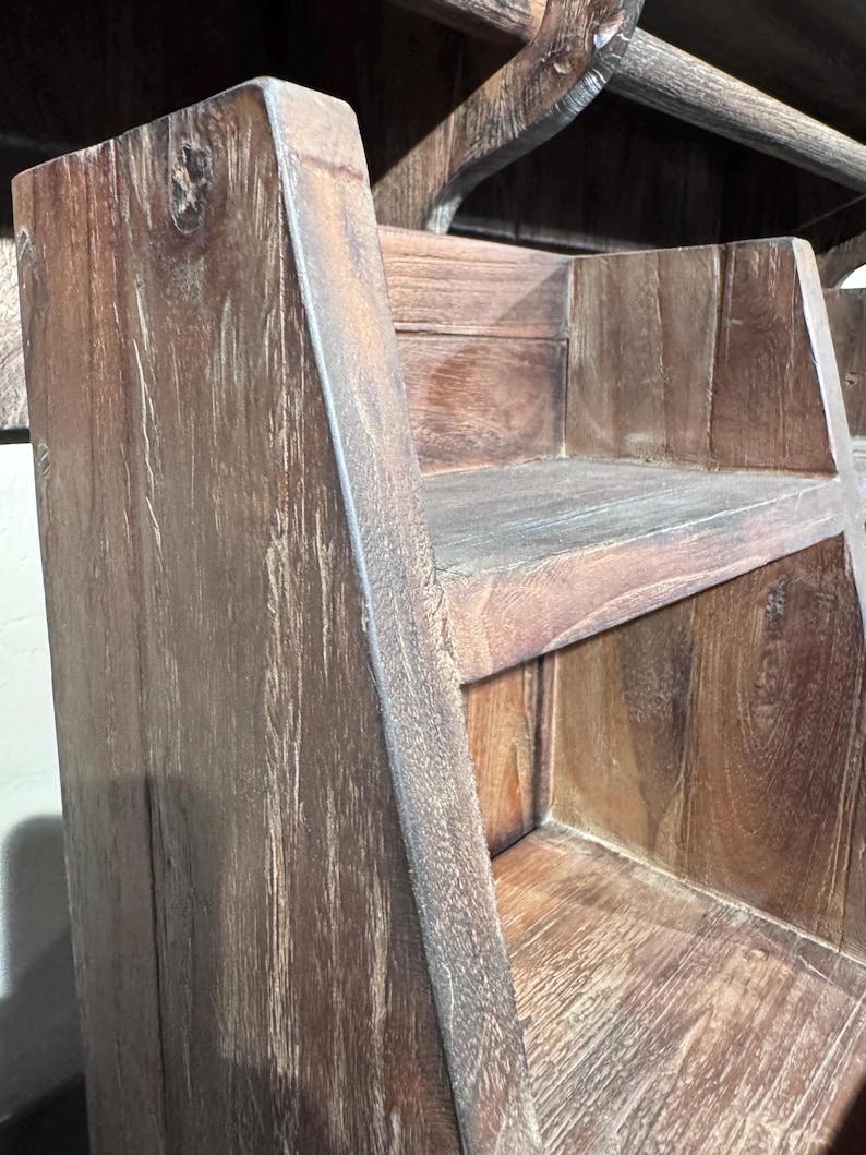 May include: A tiered wooden shelf unit featuring a dark brown finish with visible wood grain patterns. The structure consists of two open shelves with angled side panels, showcasing a rustic texture and a sturdy, multi-level design for storage.