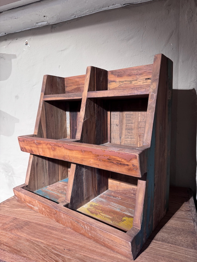 May include: A tiered wooden display shelf featuring two levels with two open compartments on each level. The structure is crafted from reclaimed wood with visible grain, brown tones, and subtle hints of blue and yellow paint on the base.