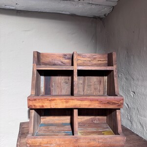 May include: A wooden storage rack featuring four open compartments arranged in two tiers. The structure is crafted from dark brown wood with visible grain patterns and subtle hints of blue and yellow paint on the lower shelf surfaces.
