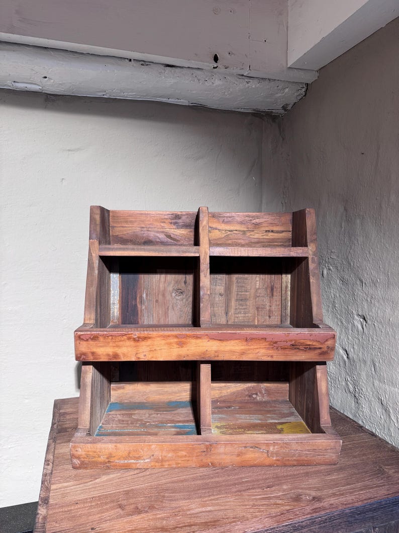 May include: A wooden storage rack featuring four open compartments arranged in two tiers. The structure is crafted from dark brown wood with visible grain patterns and subtle hints of blue and yellow paint on the lower shelf surfaces.