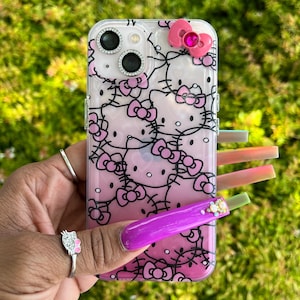 Puede incluir: Una funda transparente para tel&eacute;fono con un dise&ntilde;o de Hello Kitty rosa y negro. La funda tiene un lazo rosa con un strass en la parte superior.