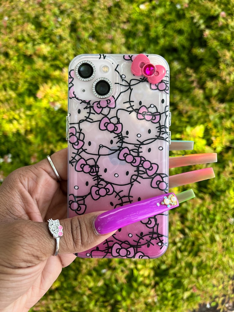 Puede incluir: Una funda transparente para tel&eacute;fono con un dise&ntilde;o de Hello Kitty rosa y negro. La funda tiene un lazo rosa con un strass en la parte superior.