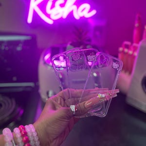 May include: Three clear phone cases with a Hello Kitty design. The cases are stacked on top of each other and are being held in a hand.