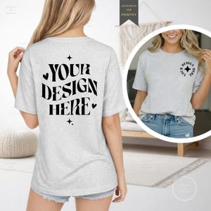 May include: A light gray t-shirt with the text "YOUR DESIGN HERE" in black script on the back. The shirt has a crew neck and short sleeves. A smaller image of the shirt is shown in a circle on the right, with the text "DESIGN HERE" on the front.