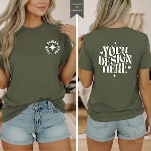 May include: An olive green t-shirt featuring white text and graphics. The front displays a small circular logo with a star and the text "YOUR DESIGN HERE." The back features a larger, wavy-font graphic reading "YOUR DESIGN HERE" with small hearts.