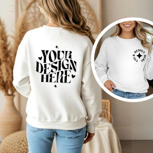 Può includere: Una felpa bianca a maniche lunghe con la scritta nera YOUR DESIGN HERE sul retro in un carattere ondulato con piccoli accenti a forma di stella e cuore. Un inserto circolare mostra la parte anteriore della felpa con un piccolo logo a stella.