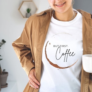May include: White t-shirt with a brown coffee stain ring and the text "BUT FIRST. Coffee" in black.
