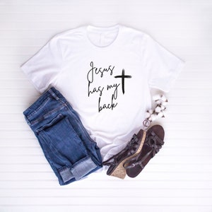 May include: White t-shirt with the text "Jesus has my back" and a black cross.