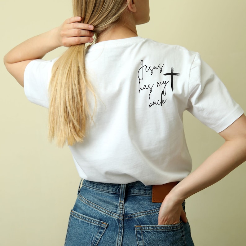 May include: White t-shirt with the text "Jesus has my back" and a black cross.