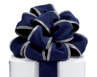 May include: A large, navy blue bow with silver trim sits atop a white gift box. The bow is made of a soft, velvety material and is intricately looped. The silver trim adds a touch of elegance to the overall design, making it suitable for various occasions.