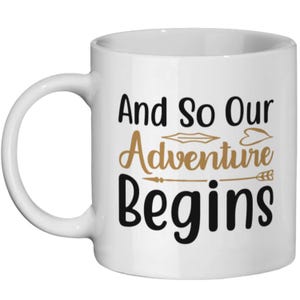 Puede incluir: Taza de café de cerámica blanca con texto negro que dice "And So Our Adventure Begins". El texto está decorado con flechas y corazones dorados.