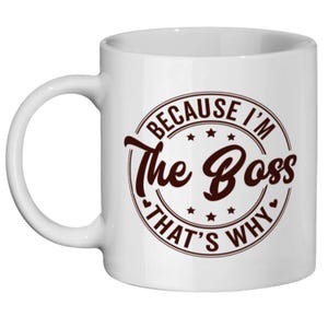 Könnte beinhalten: Weißer Keramikbecher mit gebogenem Henkel. Der Becher hat ein braunes, kreisförmiges Design mit dem Text "BECAUSE I'M The Boss THAT'S WHY". Das Design enthält Sterne und Herzen.
