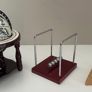 May include: A collection of educational and decorative items. Includes a globe on a wooden stand, a Newton's cradle with silver spheres, and a wooden peg game with colorful pegs.