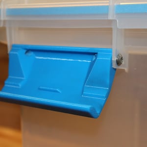 Könnte beinhalten: Nahaufnahme eines blauen Kunststoffverschlusses an einem durchsichtigen Kunststoffbehälter. Der Verschluss ist mit einer silbernen Schraube am Behälter befestigt.