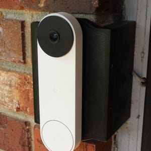 May include: A white and black smart doorbell mounted on a brick wall. The doorbell has a circular camera lens and a white, elongated body. It is installed on a black mounting bracket.