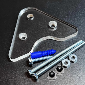 May include: A clear acrylic mounting bracket with three holes, accompanied by screws, nuts, and a blue wall anchor. The hardware is arranged on a dark surface, showcasing the components for installation.